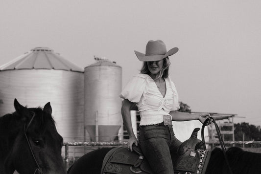 A cowgirl in a white blouse, jeans, and Western boots mounted on a horse at Highbrow Ranch in Caldwell, Texas — from our guide to the best Ariat western boots